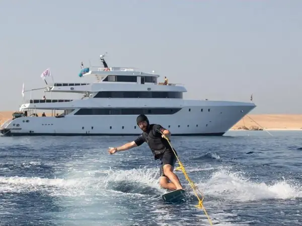 Wakeboarder riding behind a boat near a white yacht